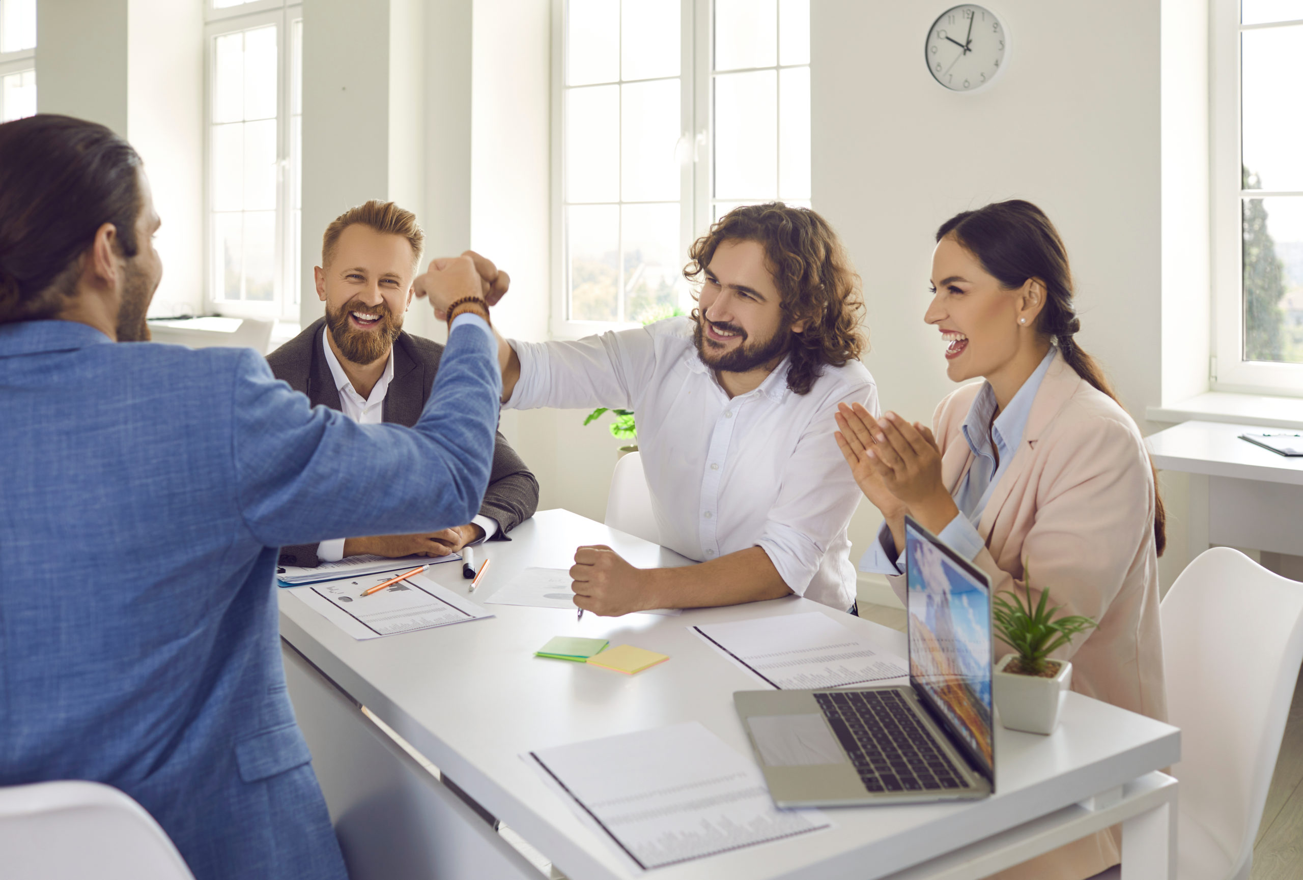 happy business people sitting at an office desk and fist bumping after making a deal